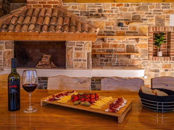 A wooden table with a charcuterie board, a bottle of wine, and a glass of red wine.