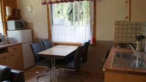 Eine kompakte Küche mit Esstisch, Stühlen, einer Mikrowelle, einer Kaffeemaschine und einem Fenster mit Vorhängen.