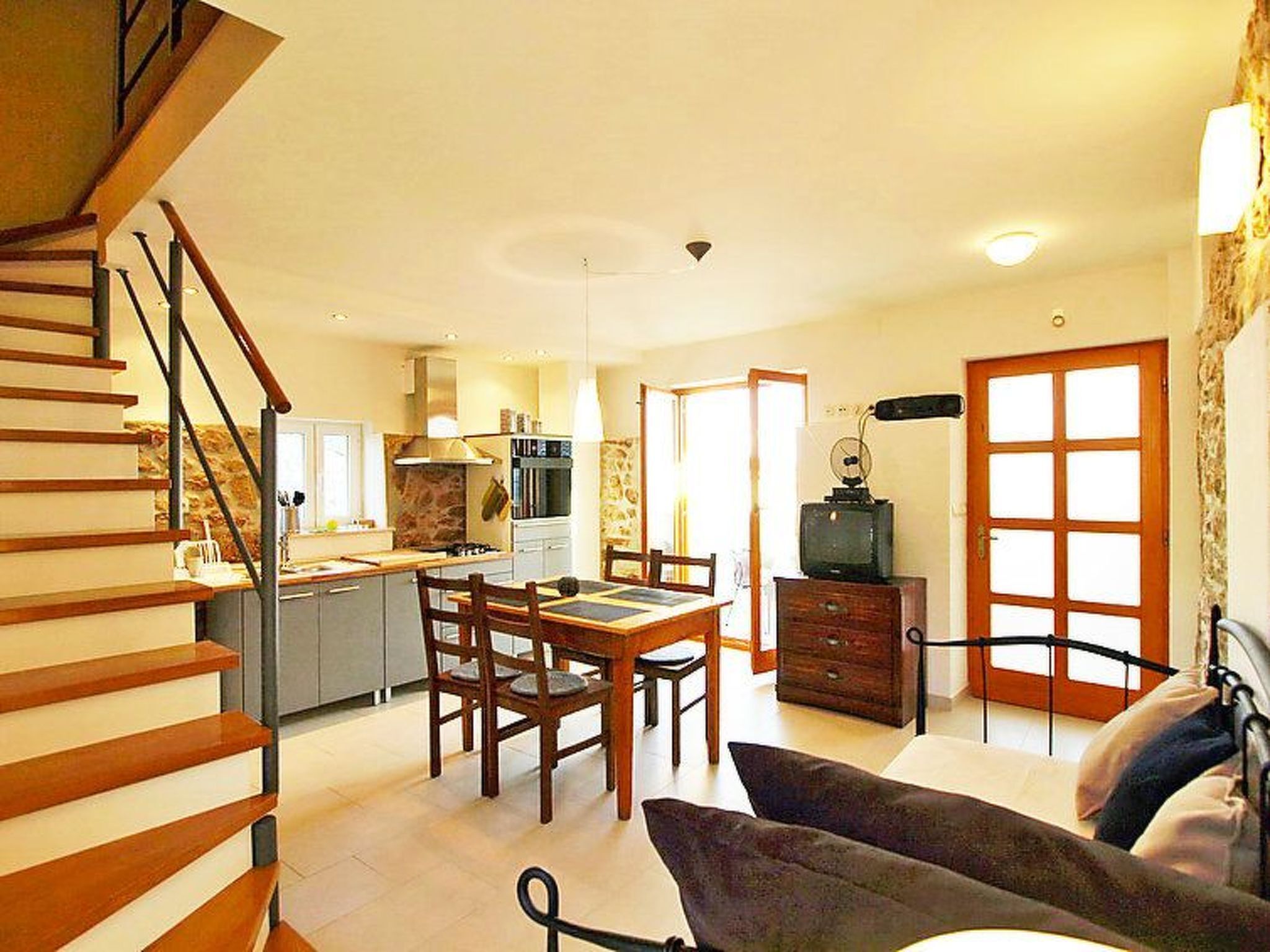 A spacious living area with a dining table, chairs, a sofa, and a staircase.