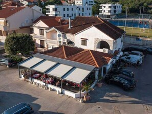 Un bâtiment doté d’un toit recouvert de tuiles, d’un espace extérieur abrité avec des sièges et d’un parking où sont garées des voitures.