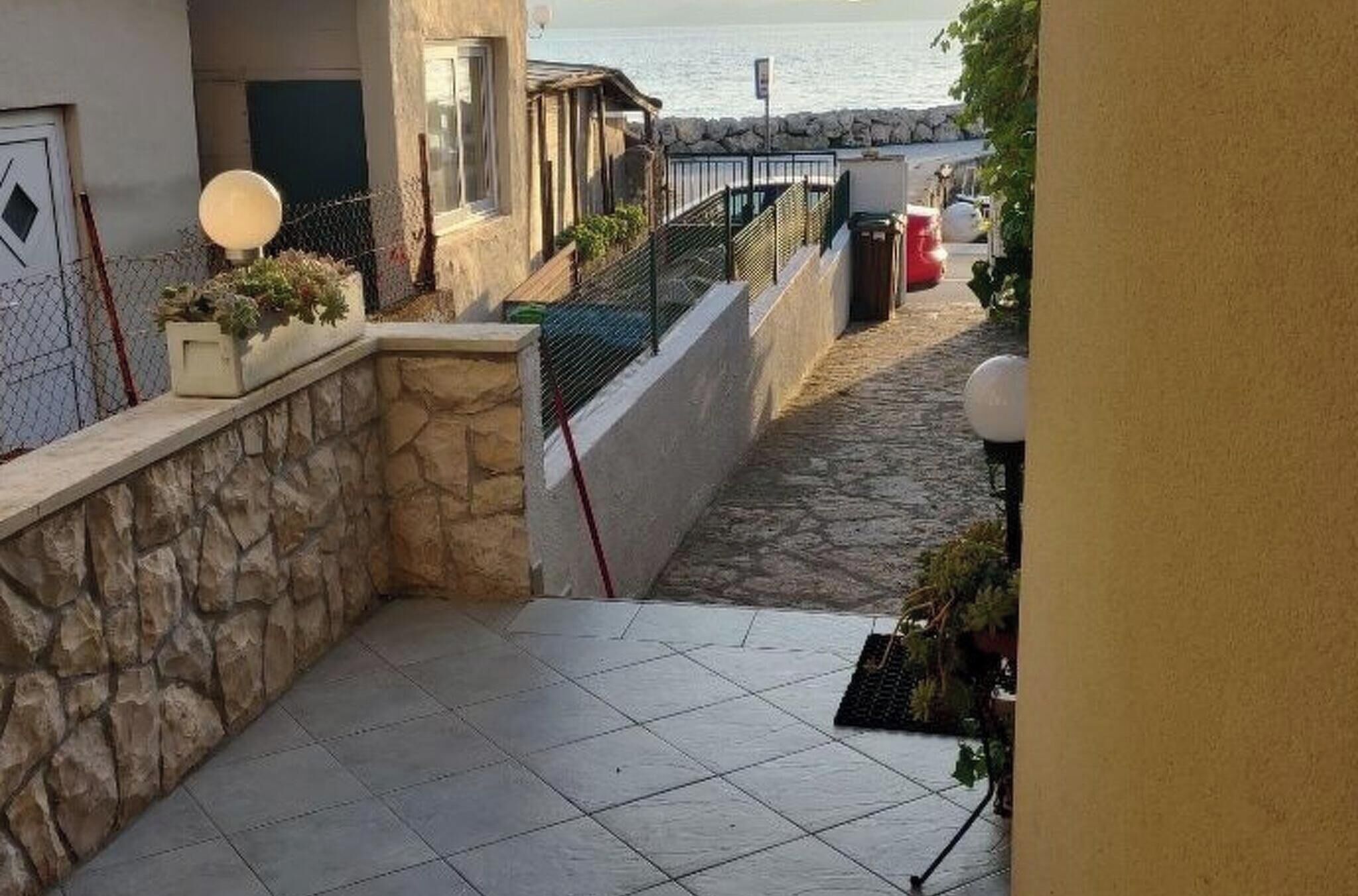 A narrow stone pathway leading to a balcony overlooking a body of water, with a stone wall on one side and a fence on the other.