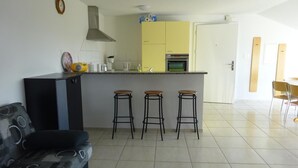 Eine moderne Küche mit einer zentralen Kochinsel, drei Barhocker, einer Couch und einem Essbereich mit Stühlen.