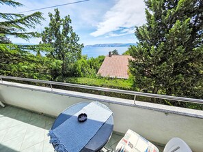 A balcony with a table, a chair, and a view of a house and mountains. - Appartement mit Balkon und Meerblick by Interhome (Novi Vinodolski)