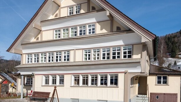 A multi-story building with a symmetrical facade, large windows, and a prominent central entrance. - Lindeli by Interhome (St. Peterzell)