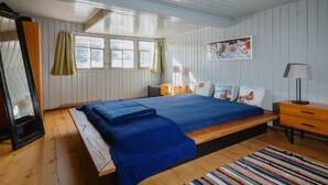 A bedroom with a large bed, wooden floor, a window with curtains, a painting on the wall, and a nightstand. - Lindeli by Interhome (St. Peterzell)