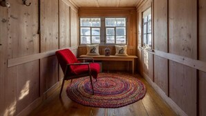A cozy cabin interior with wooden walls, a bench with cushions, a red chair, and a colorful rug. - Lindeli by Interhome (St. Peterzell)