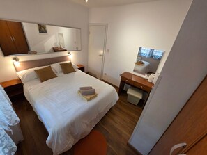 A neatly arranged hotel room with a large bed, a bedside table with a lamp, a small desk with a mirror, and a wardrobe. - Wohnung mit Terrasse - Gemeinschaftspool by Interhome (Novi Vinodolski)