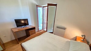 Et soveværelse med en træseng, et skrivebord med tv, en radiator og et vindue med rullegardiner.