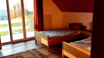 Une chambre avec deux lits simples, une grande fenêtre donnant sur un jardin et un plafond en bois.