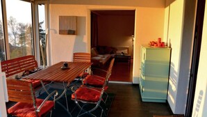 Een gezellige woonkamer met een houten eettafel, rode fauteuils, een bank en een lichtblauwe koelkast.