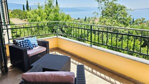 A balcony with wicker furniture, a yellow wall, and a view of greenery and mountains. - Wohnung für 6 Personen, 150m vom Strand entfernt by Interhome (Novi Vinodolski)