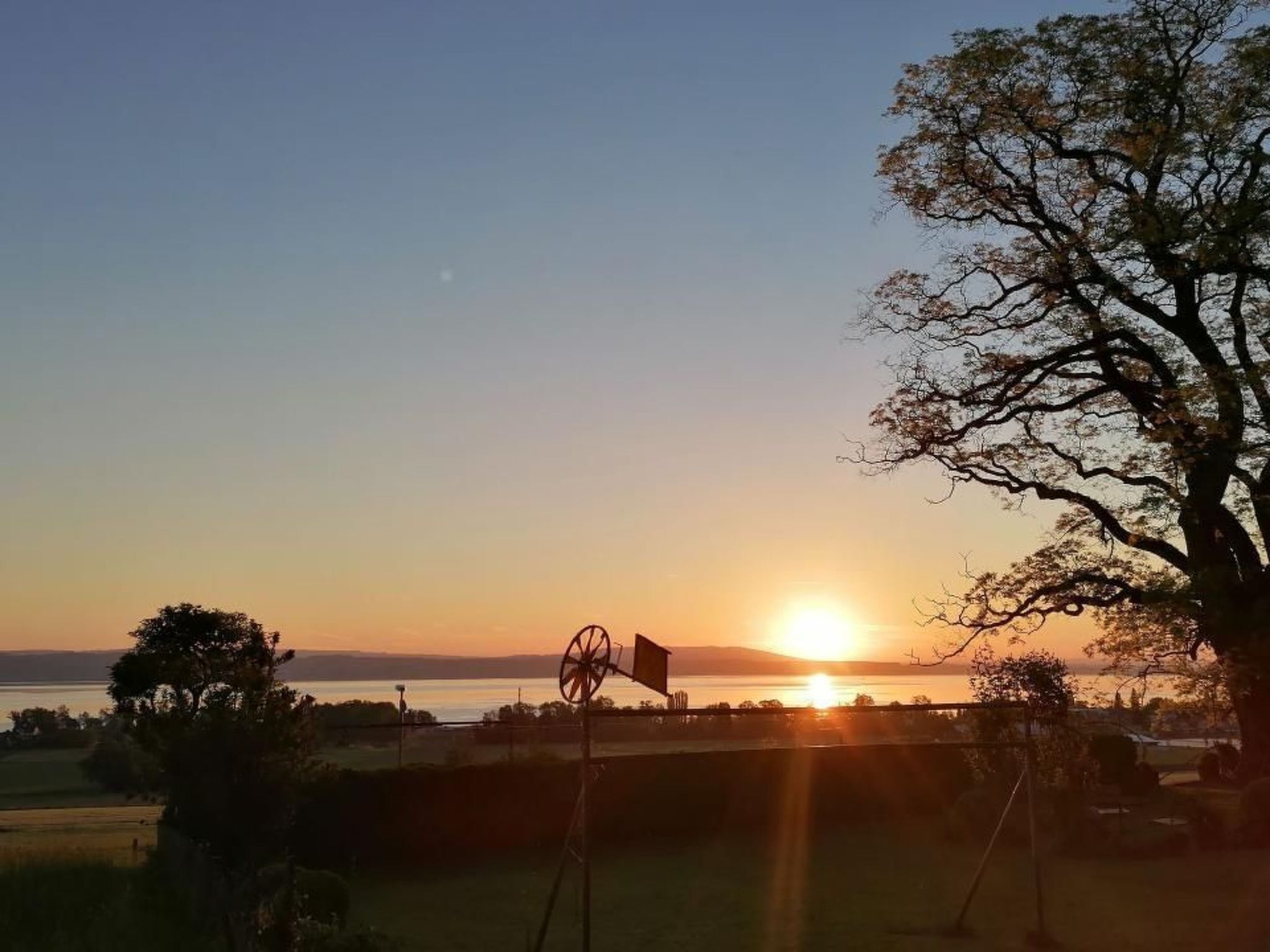 Ein Sonnenuntergang über einem Gewässer, im Vordergrund eine Windmühle.