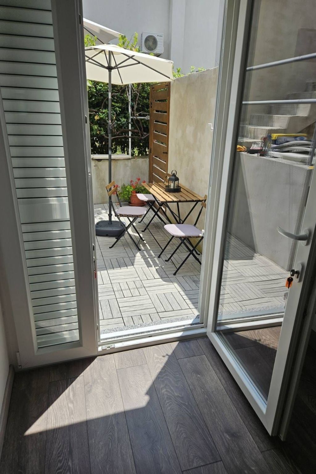 Eine moderne Terrasse mit einem Holztisch und Stühlen, einem Topfpflanzen und einem weißen Sonnenschirm.
