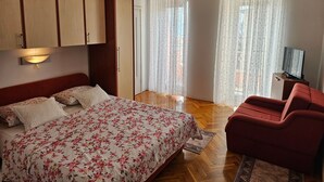 A bedroom with a bed, a red chair, a TV on a wooden cabinet, and a window with curtains. - Studio-Wohnung in Novi Vinodolski by Interhome (Novi Vinodolski)