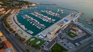 An aerial view of a marina with boats docked, a road leading to the marina, and a building with a blue roof. - Studio-Wohnung in Novi Vinodolski by Interhome (Novi Vinodolski)