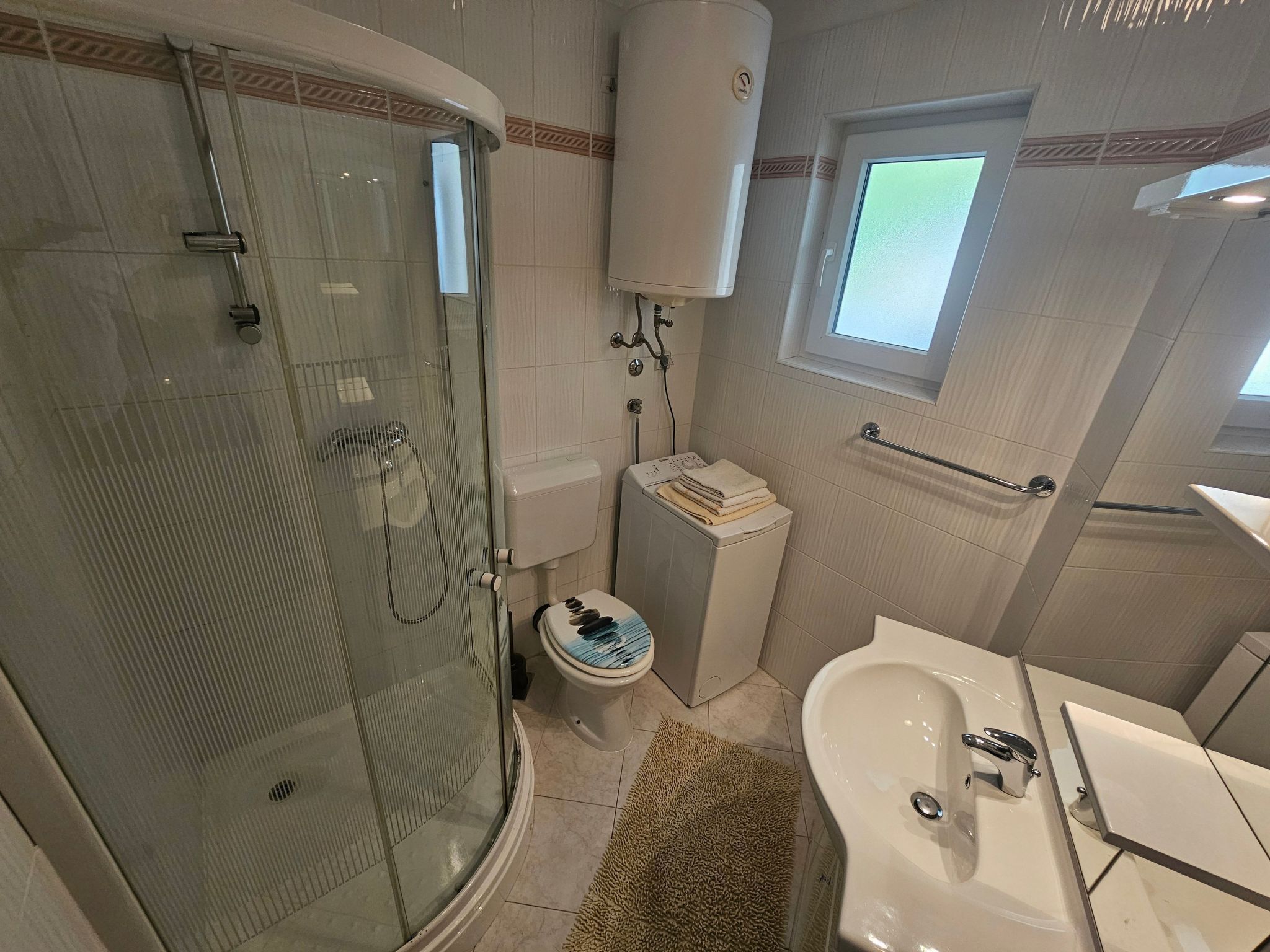 A bathroom with a glass-enclosed shower, a toilet, a sink, and a window.