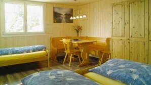 Ein Zimmer mit zwei Einzelbetten, einem Holztisch mit Stuhl, einem Fenster und einer Wandlampe.