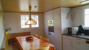 Eine Küche mit Holzbalkendecke, einem Tisch mit Stühlen, einer Hängelampe und einer Mikrowelle.