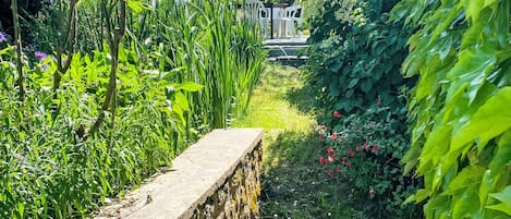 A garden pathway with a stone wall, lush greenery, and a wooden bench.