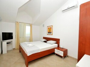 A bedroom with a wooden bed, a bedside table, a TV, and an air conditioning unit. - Villa Luna 3 by Interhome (Trogir/Okrug Donji)