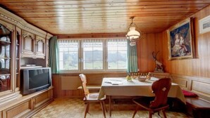 Zona de menjador amb taula de fusta, cadires, un penjallum i un televisor.