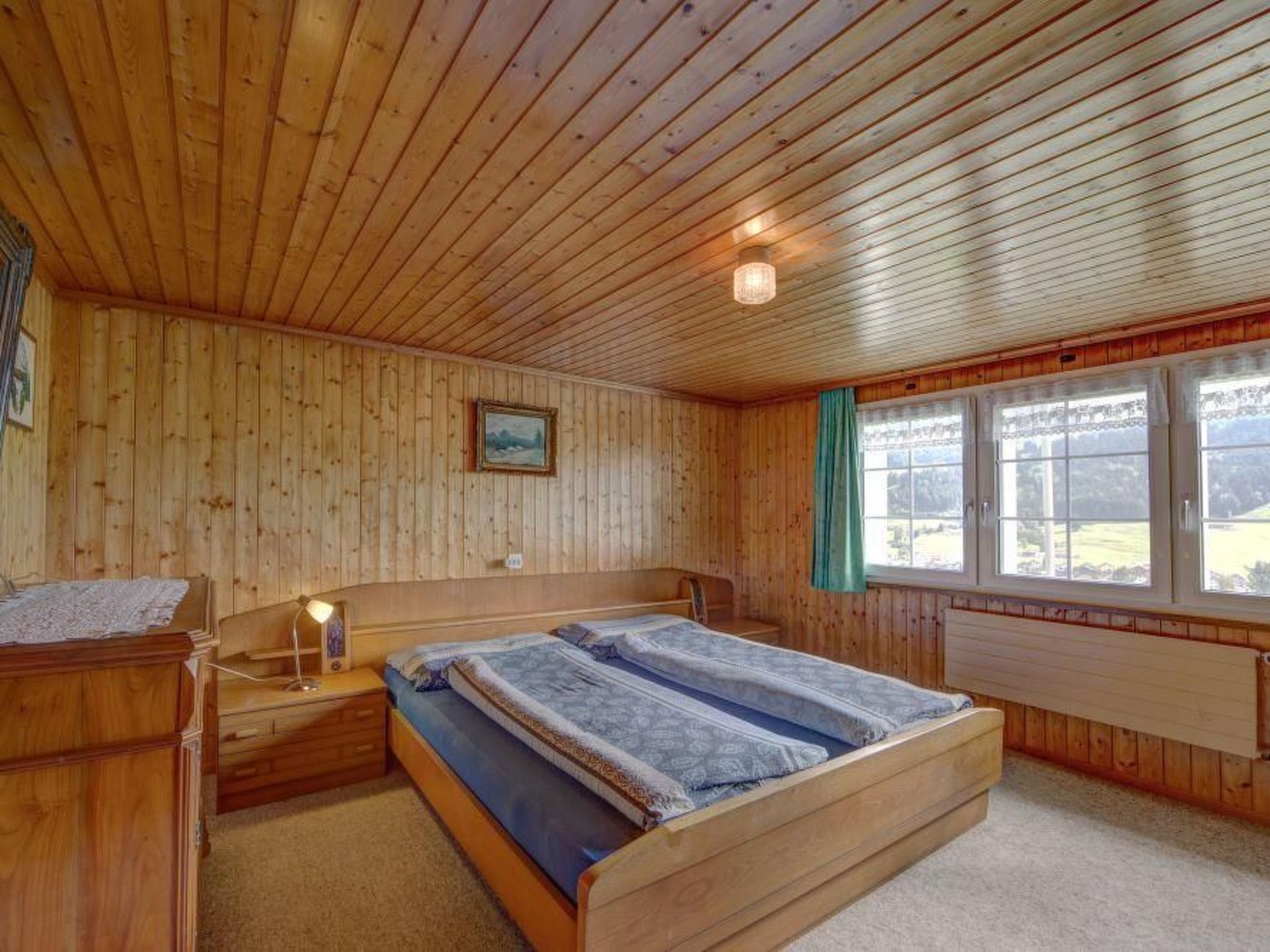 Una habitación con paneles de madera, una cama, una mesita de noche, una lámpara y un ventanal con cortinas.