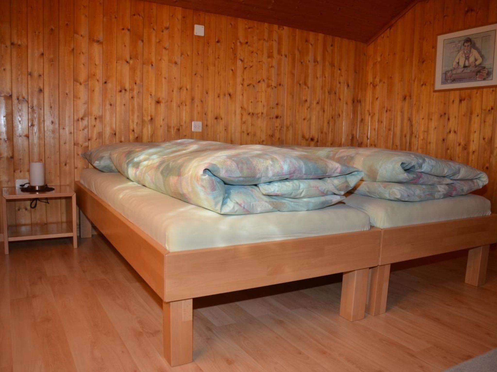 Una habitación con paneles de madera, una cama, una mesita de noche y un interruptor de luz en la pared.