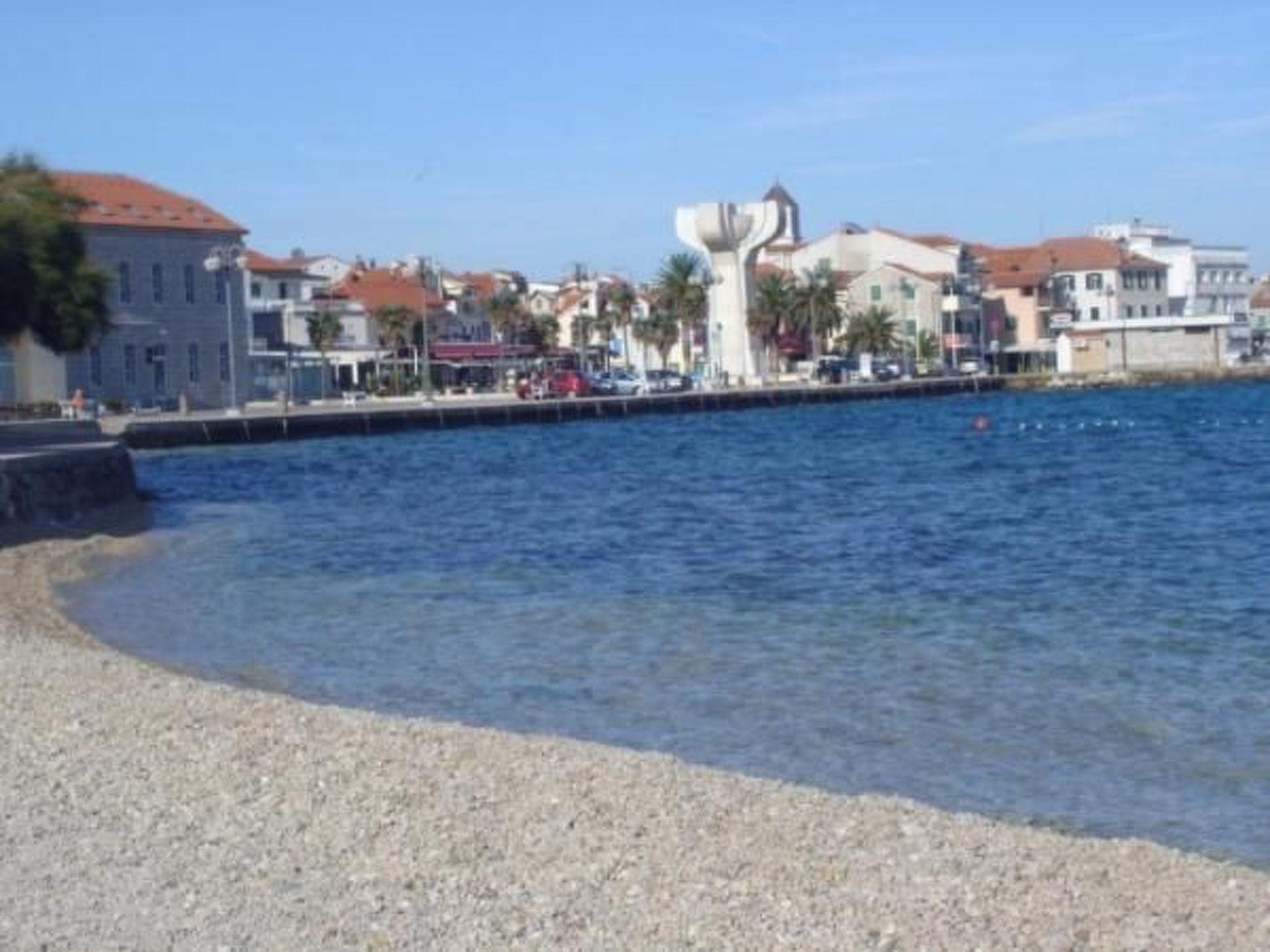 Une zone côtière bordée de bâtiments le long du littoral, une plage de galets et un ciel bleu dégagé.