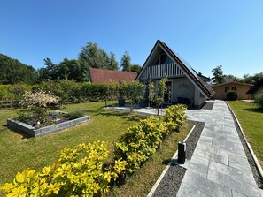 Ein modernes Haus mit einem geneigten Dach, einer gepflasterten Auffahrt und einem gepflegten Garten mit gelb blühenden Pflanzen.