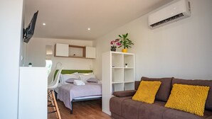 A modern hotel room with a bed, a brown sofa, a white shelving unit, and a mounted TV. - Mobilheim direkt am Strand by Interhome (Ugljan/Ugljan)