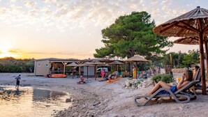 A beachside setting with a small building, umbrellas, and lounge chairs. - Mobilheim direkt am Strand by Interhome (Ugljan/Ugljan)