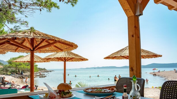 A beachside restaurant with outdoor seating, umbrellas, and a view of the sea. - Mobilheim direkt am Strand by Interhome (Ugljan/Ugljan)