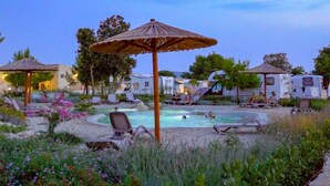 A pool area with lounge chairs and umbrellas, surrounded by greenery and trees. - Mobilheim direkt am Strand by Interhome (Ugljan/Ugljan)