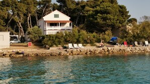 Una propiedad costera con un edificio blanco, un muro de piedra y una fila de sillas de playa.