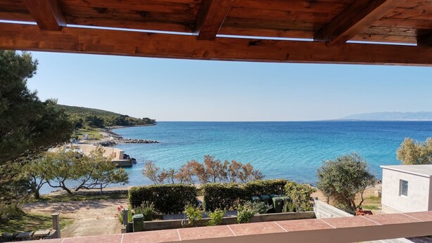 Un balcón con vistas a un paisaje costero, que incluye un mar azul cristalino y un fondo montañoso.