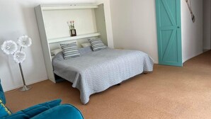A bedroom with a bed, a white bedside table, a teal door, and a floor lamp. - South Beach Apartment 10km Rheinfall by Interhome (Hemmental)