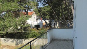 Un balcon doté d’une rambarde en métal, d’un sol en gravier et offrant une vue sur un immeuble avec un toit rouge et une façade blanche.