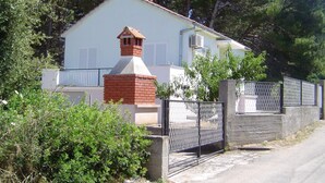 Une maison avec une cheminée en briques, une entrée fermée par un portail et une façade blanche.