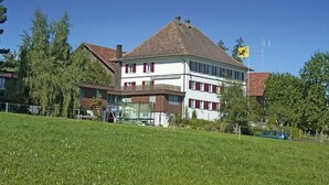 Een gebouw met twee verdiepingen, een schuin dak, rode luiken en een vlag aan de rechterkant.
