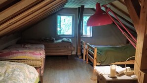 Un dormitorio ático acogedor con dos camas, piso de madera, una lámpara de escritorio roja y una ventana que proporciona luz natural.