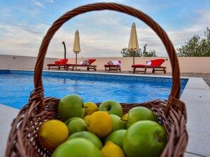 A swimming pool with lounge chairs and umbrellas, and a basket of green and yellow fruits in the foreground. - Villa Maslina mit privatem Pool in ruhiger Lage by Interhome (Nin)