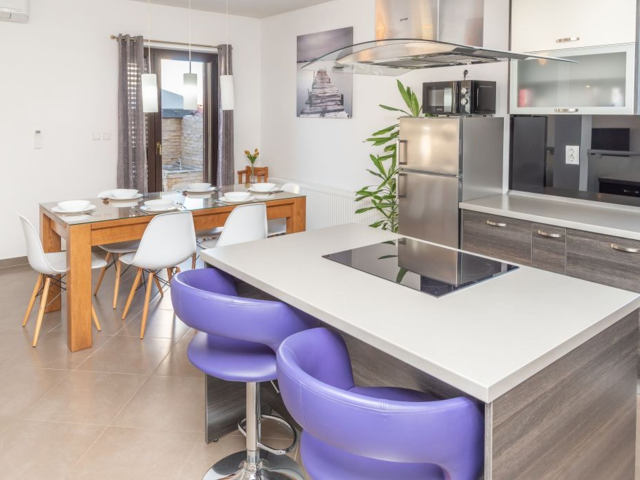 A modern kitchen with a central island, bar stools, and a dining area with a table and chairs.