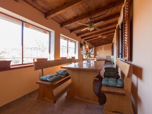A spacious room with wooden benches and a central island, large windows with blinds, and a ceiling fan. - "Jasmin" by Interhome (Nin)