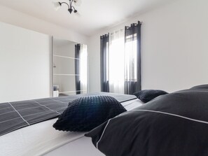 A modern bedroom with a bed, a large mirror, and a window with curtains. - "Jasmin" by Interhome (Nin)