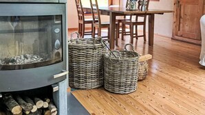 A rustic interior with a wood-burning stove, a dining table with chairs, wicker baskets, and a wooden ceiling.