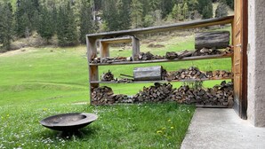 A rustic outdoor area with a fire pit, stacked firewood, and a wooden structure.