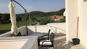 A balcony with a table and chairs, a white umbrella, and a view of a green landscape with hills. - The Blue Line Ferienwohnung mit Balkon by Interhome (Rab/Kampor)