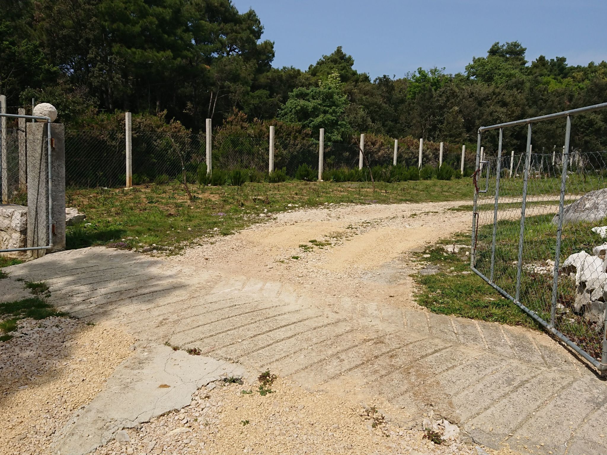 Ein Kiesweg führt zu einem umzäunten Bereich mit einem Tor.