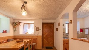 A cozy dining area with a wooden table and chairs, a window with curtains, and a wooden door leading to the kitchen. - Chalet Chiara by Interhome (Casaccia)