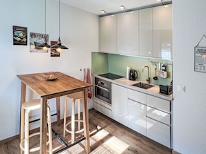 A compact kitchen with a wooden table, bar stools, a coffee maker, and a kettle.